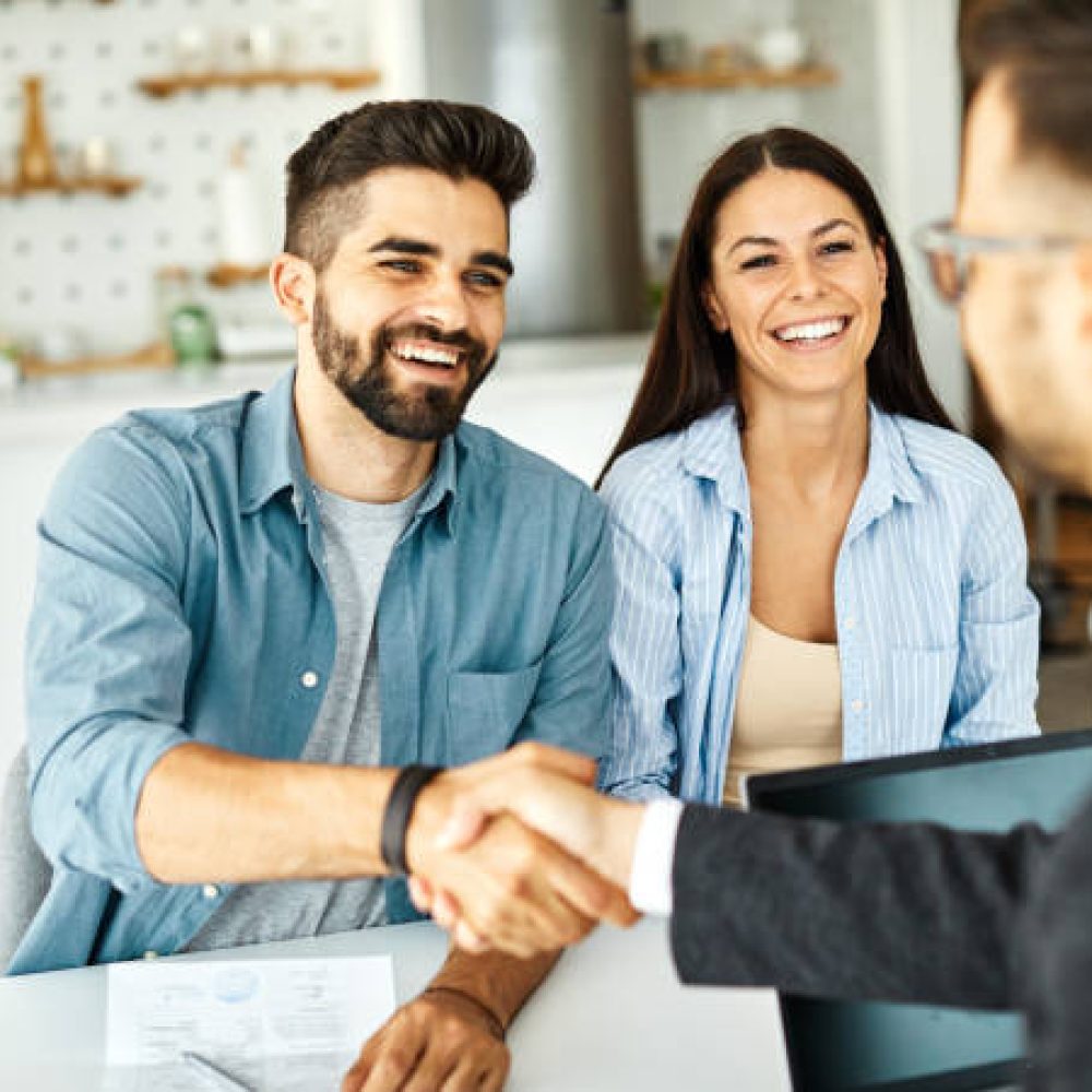 Real estate agent with couple shaking hands closing a deal and signing a contract